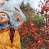 Smiling woman holding umbrella near tree in autumn park